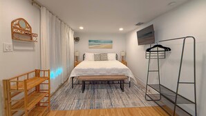 Un dormitorio con cama, un banco de madera, un televisor y un perchero.