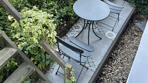 Eine Terrasse mit einem runden Tisch und Bänken, umgeben von Grünpflanzen und Topfpflanzen.