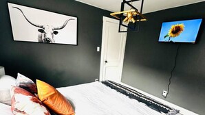 Une chambre à coucher avec un lit, des oreillers, un téléviseur fixé au mur et un luminaire au plafond.