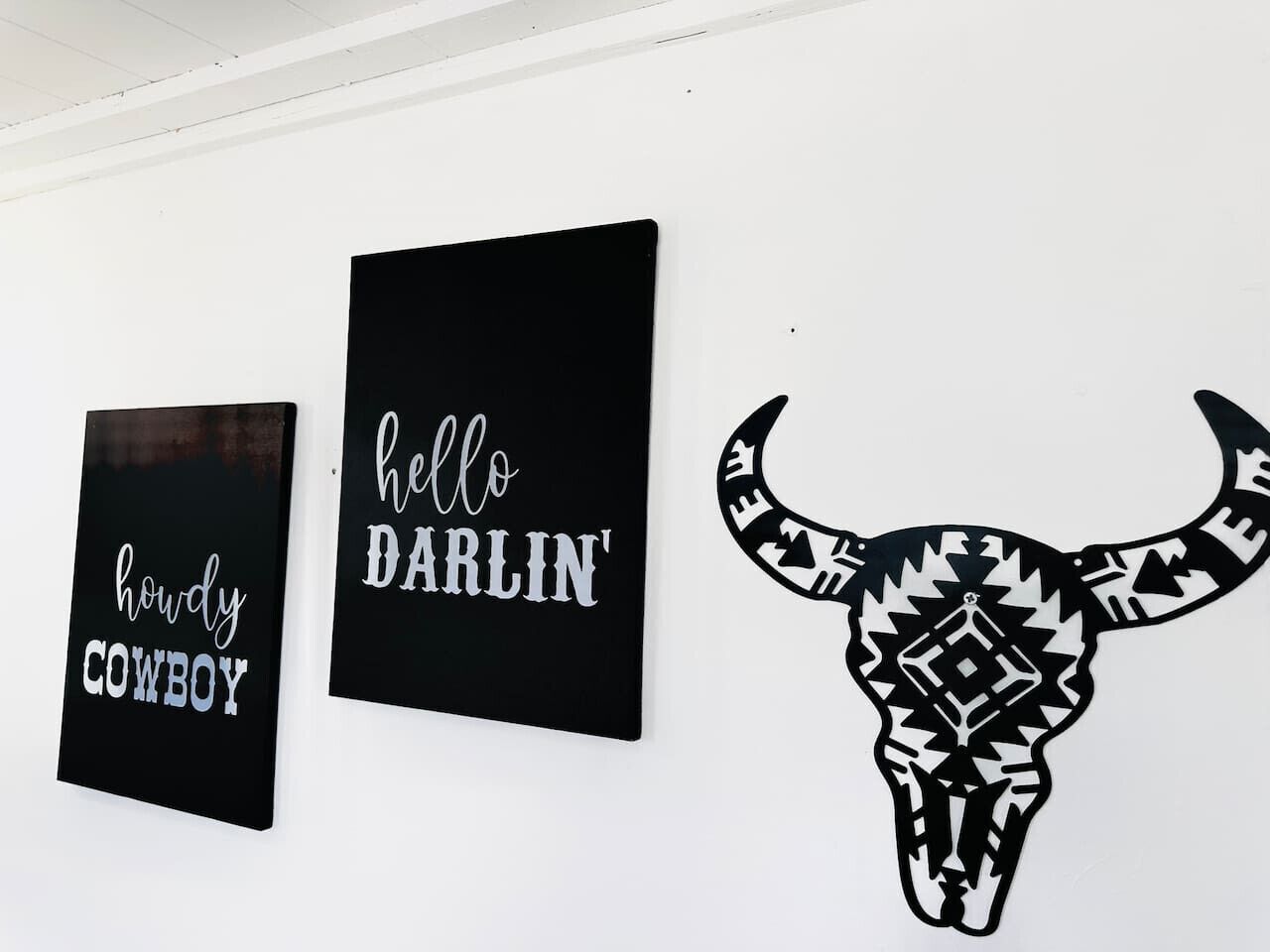 Tres quadres en blanc i negre: un senyal amb tema de cowboys, un senyal que diu 'hello DARLIN' i una representació estil·litzada d'una cabeça de bou.