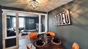 Un coin repas avec une table ronde dressée pour quatre personnes, agrémenté d’assiettes noires et de chaises orange.
