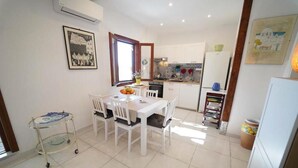 A dining area with a white table and chairs, a small cart, and a kitchen in the background. - Charming Chalet Trilocale Located in Forio d'Ischia a few steps from the sea (Forio)