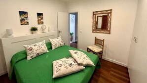 A bedroom with a green bedspread, two wall-mounted paintings, a mirror, and a wooden chair. - Charming Chalet Trilocale Located in Forio d'Ischia a few steps from the sea (Forio)