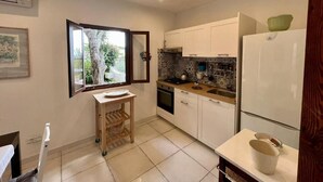A compact kitchen with white cabinets, a built-in oven, a sink, and a window with a view of greenery. - Charming Chalet Trilocale Located in Forio d'Ischia a few steps from the sea (Forio)