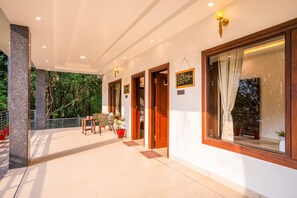 A covered outdoor area with a seating arrangement, wooden doors, and a view of greenery. - Moustache Select Naukuchiatal By the Lake (Nainital)
