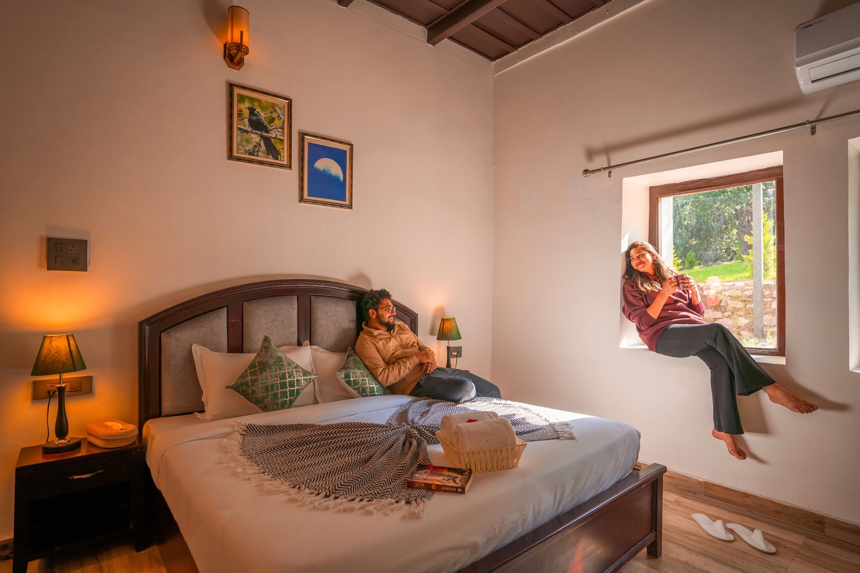 A bedroom with a bed, bedside lamps, a window, and a wall with two framed pictures.