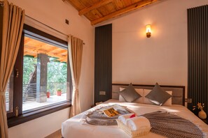 A bedroom with a large bed, a window with curtains, a wall-mounted light, and a view of greenery outside. - Moustache Select Naukuchiatal By the Lake (Nainital)
