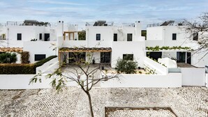 A modern building with multiple white structures, a covered outdoor area, and a cobblestone courtyard. - Villa Serena in Santa Luzia (Tavira)