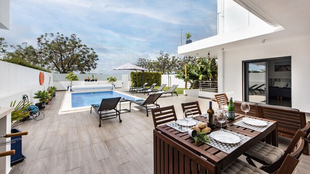 A modern outdoor patio with a pool, lounge chairs, and a dining area with a table set for two. - Villa Serena in Santa Luzia (Tavira)