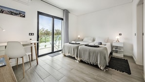 A modern bedroom with a desk, two beds, a large window, and a view of greenery. - Villa Serena in Santa Luzia (Tavira)