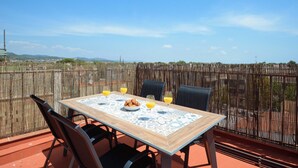 A table set with a bowl of croissants, glasses of orange juice, and a patterned tablecloth on a terrace with a bamboo fence backdrop. - Castelldefels - Apartment - Sleeps 4 - Beach Side (Castelldefels)