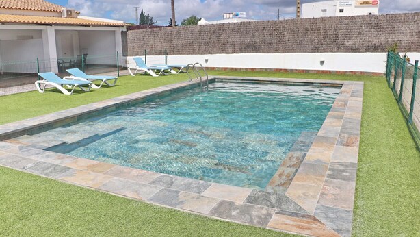 Una piscina rectangular con agua cristalina, bordeada por una piedra y césped artificial verde.