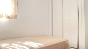 Una habitación con una cama, una ventana con cortinas de gasa y una pared de azulejos blancos.