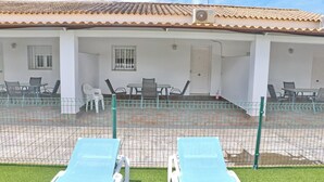 Un edificio con techo de tejas, un patio cubierto con mobiliario exterior y una piscina cercada.