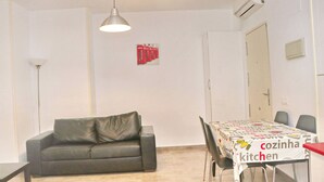 Una habitación pequeña y bien iluminada con sofá, una mesa de comedor con sillas y una zona de kitchenette.