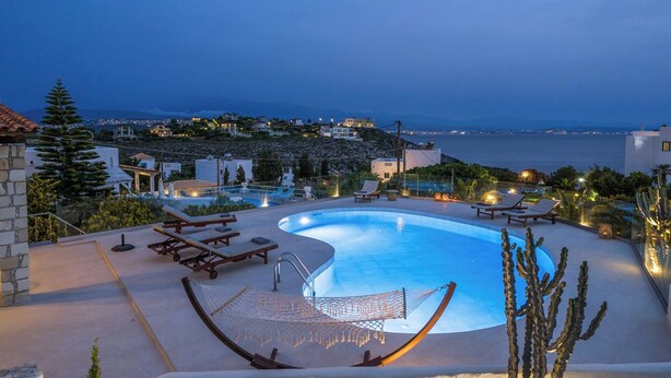 A swimming pool with lounge chairs and a hammock, surrounded by cacti and a view of the sea and town. - Luxury 3 bedroom Villa with heated pool (Akrotiri)