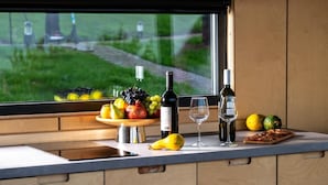 A kitchen counter with a fruit bowl, wine bottles, and glasses. - Roombox Kisiskhevi (Telavi)