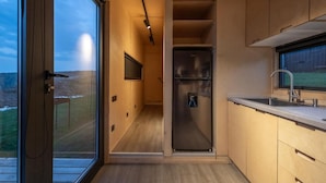 A modern kitchen with a built-in refrigerator, a sink, and a window overlooking a snowy landscape. - Roombox Kisiskhevi (Telavi)