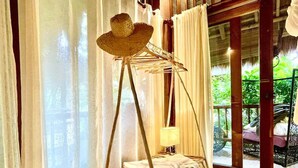 Een kamer met een hangstoel, een kleine tafel met een lamp, en uitzicht op groen buiten.