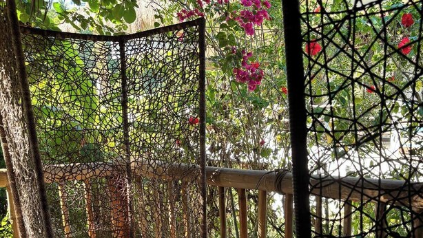 A wicker lounge chair with a cushion, a woven basket, and a bamboo fence in a garden setting. - Budget Studio with Kitchen – 4 Min to Beach (Malay)
