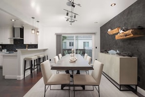 A modern kitchen with a dining area, featuring a central island, bar stools, and a large dining table.