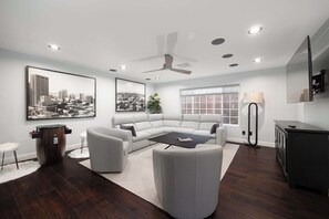 A modern living room with a sectional sofa, a round coffee table, a ceiling fan, and a large window.