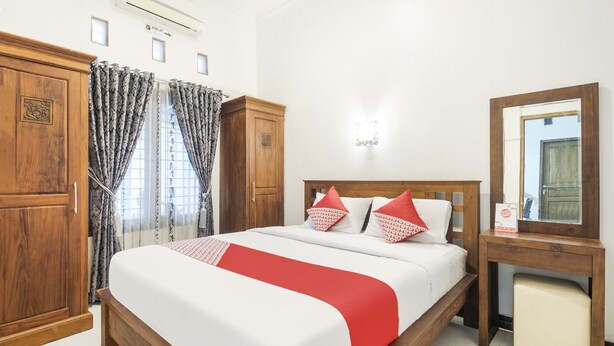 Une chambre d’hôtel avec un lit en bois, une table de chevet, un miroir et une armoire.
