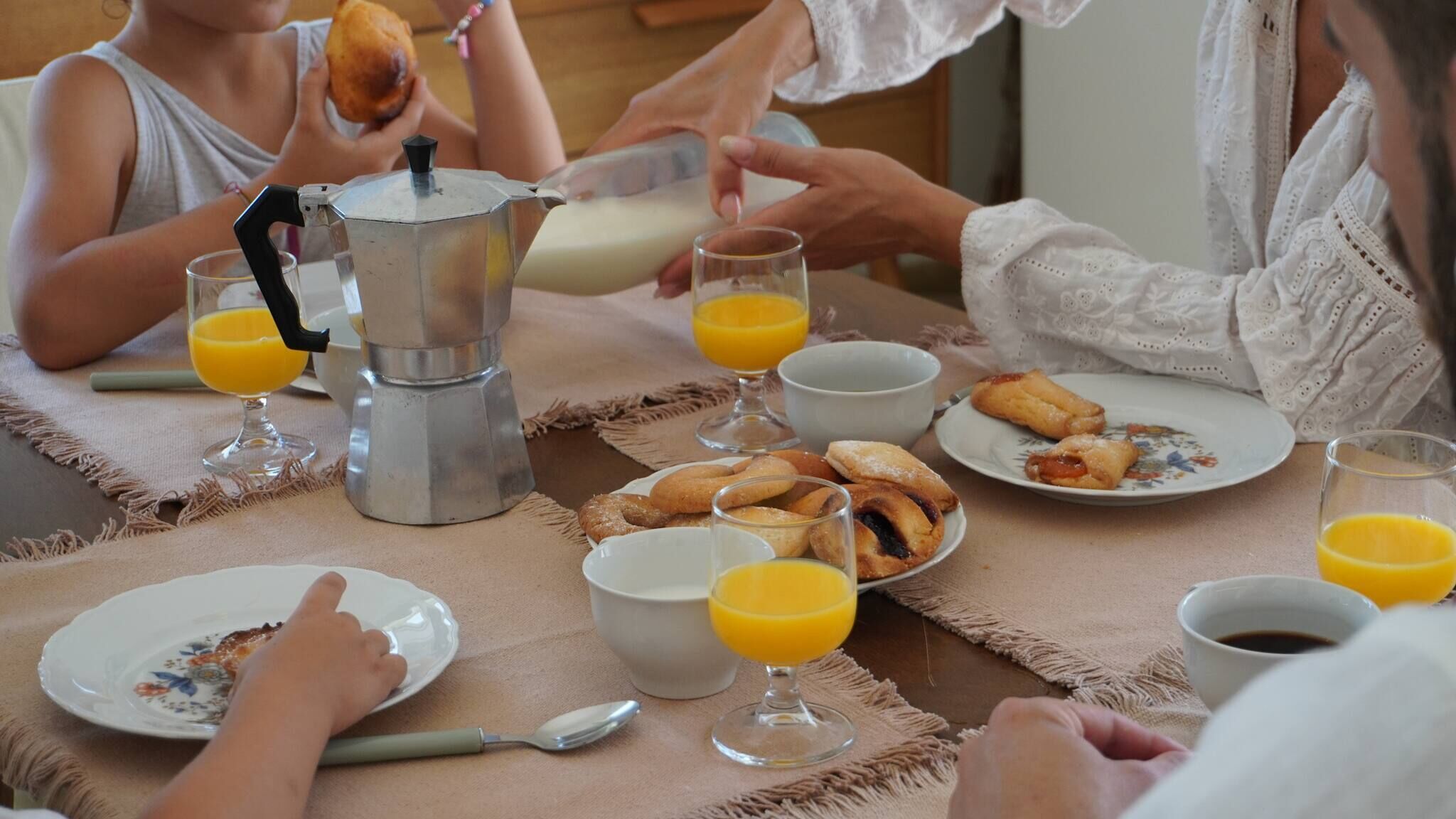 A breakfast setting with a coffee maker, plates of pastries, glasses of orange juice, and a cup of coffee.