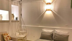Un dormitorio con una silla colgante, una cama con almohadas y una mesita de noche con lámpara.