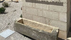 Un muro de piedra con la inscripción "MASSERIA TRE ARCHI" y un abrevadero de piedra en la base.