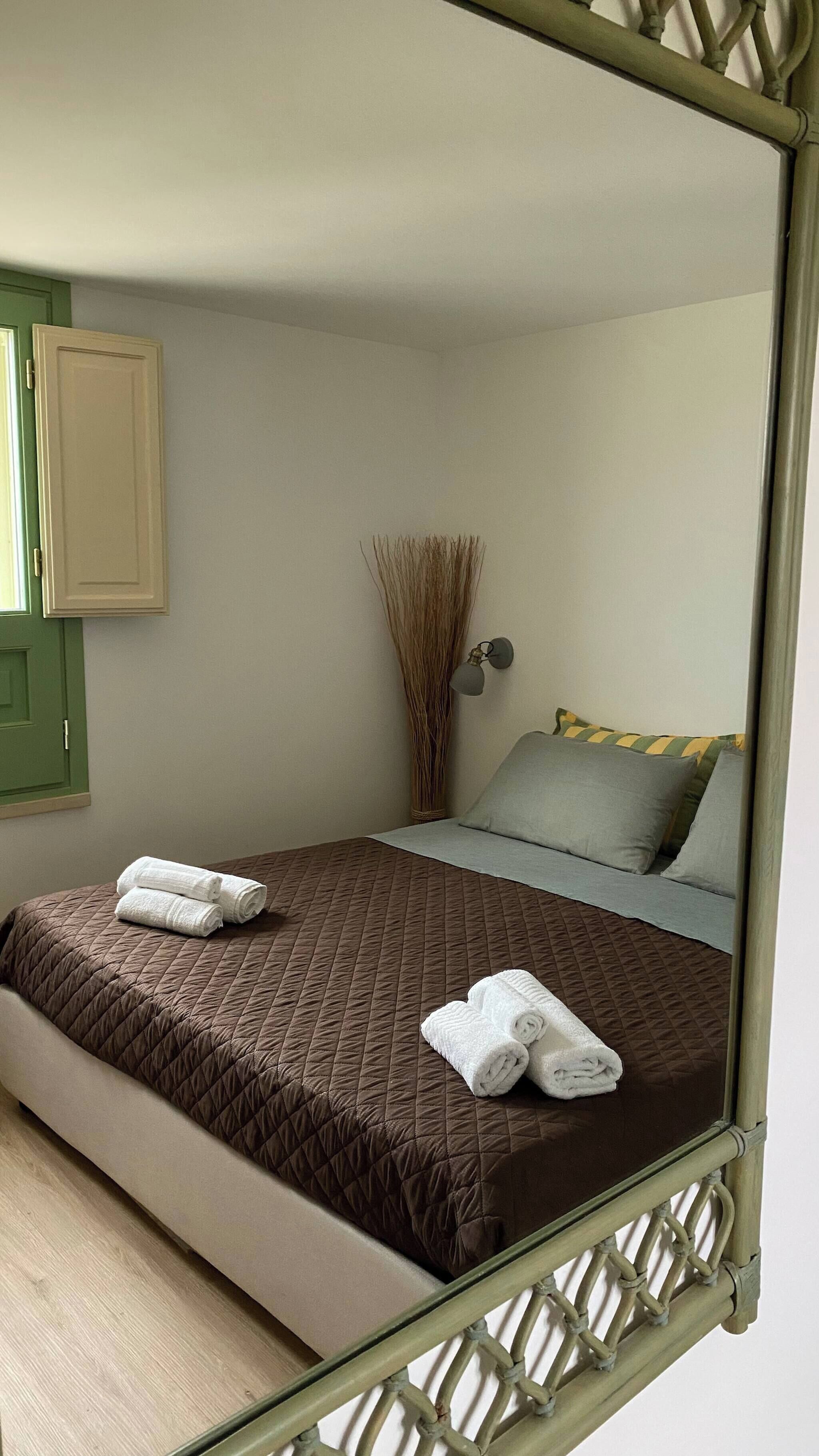 A bedroom with a bed, pillows, a vase, and a mirror.