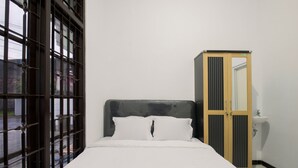 Un dormitorio con cama, armario y ventana con rejas.