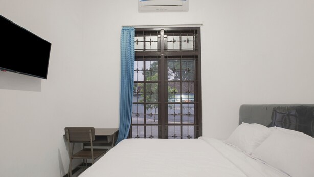Un dormitorio con cama, escritorio, silla, televisor y ventana con cortina.
