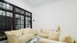 Un salón con dos sofás color crema, una mesa de centro de vidrio y un ventanal con marcos de madera oscura.