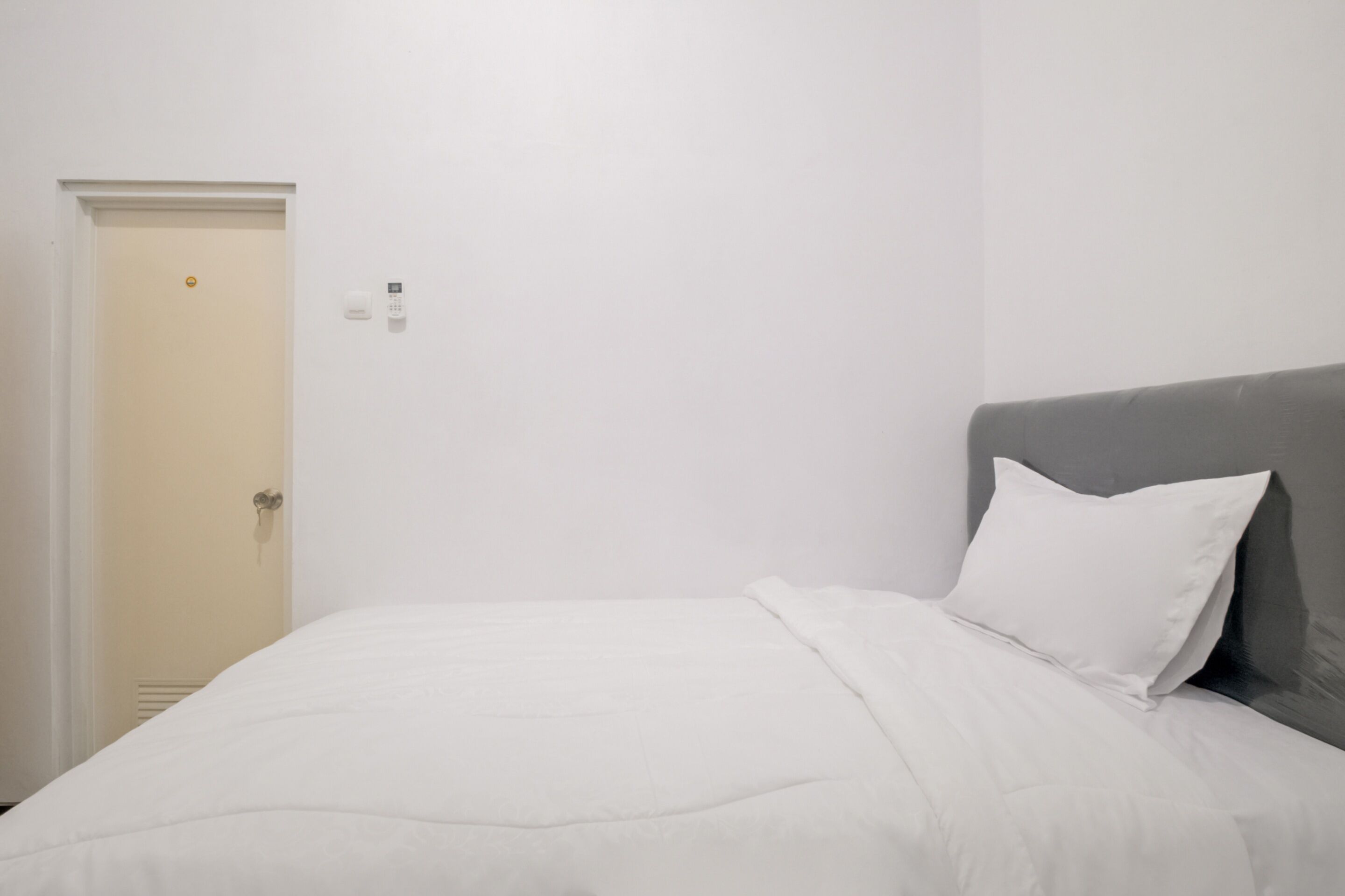 Een hotelkamer met een bed, een deur en een lichtschakelaar aan de muur.
