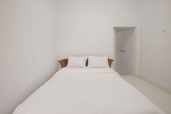A small, neatly made bed with white bedding in a minimalistic room with white walls and a wooden headboard. - OYO 3467 White Residence (Depok)