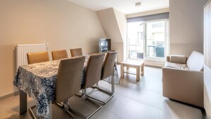 Een moderne woonkamer met een eethoek, een televisie en een groot raam met uitzicht.