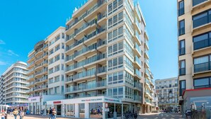 Een hotel met meerdere verdiepingen, balkons, een restaurant op de begane grond en een helderblauwe lucht.