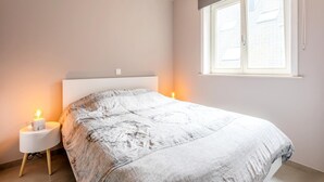 Een slaapkamer met een bed, twee bedlampjes, een raam met jaloezieën en een plafondlamp.