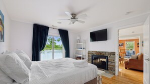 A bedroom with a bed, a ceiling fan, a fireplace, and a TV mounted on the wall.