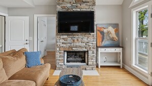 A living room with a stone fireplace, a flat-screen TV, a sofa, and a painting.