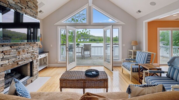 A spacious living room with a stone fireplace, a television, and a large window overlooking a deck.