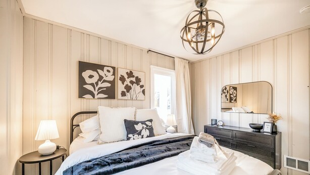 Ein ordentlich eingerichtetes Schlafzimmer mit Bett, Nachttisch, Lampe und Kommode mit Spiegel.