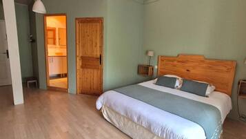 Un dormitorio con cabecera de madera, una cama grande con colcha blanca y azul, una puerta de madera y una mesita de noche con lámpara.