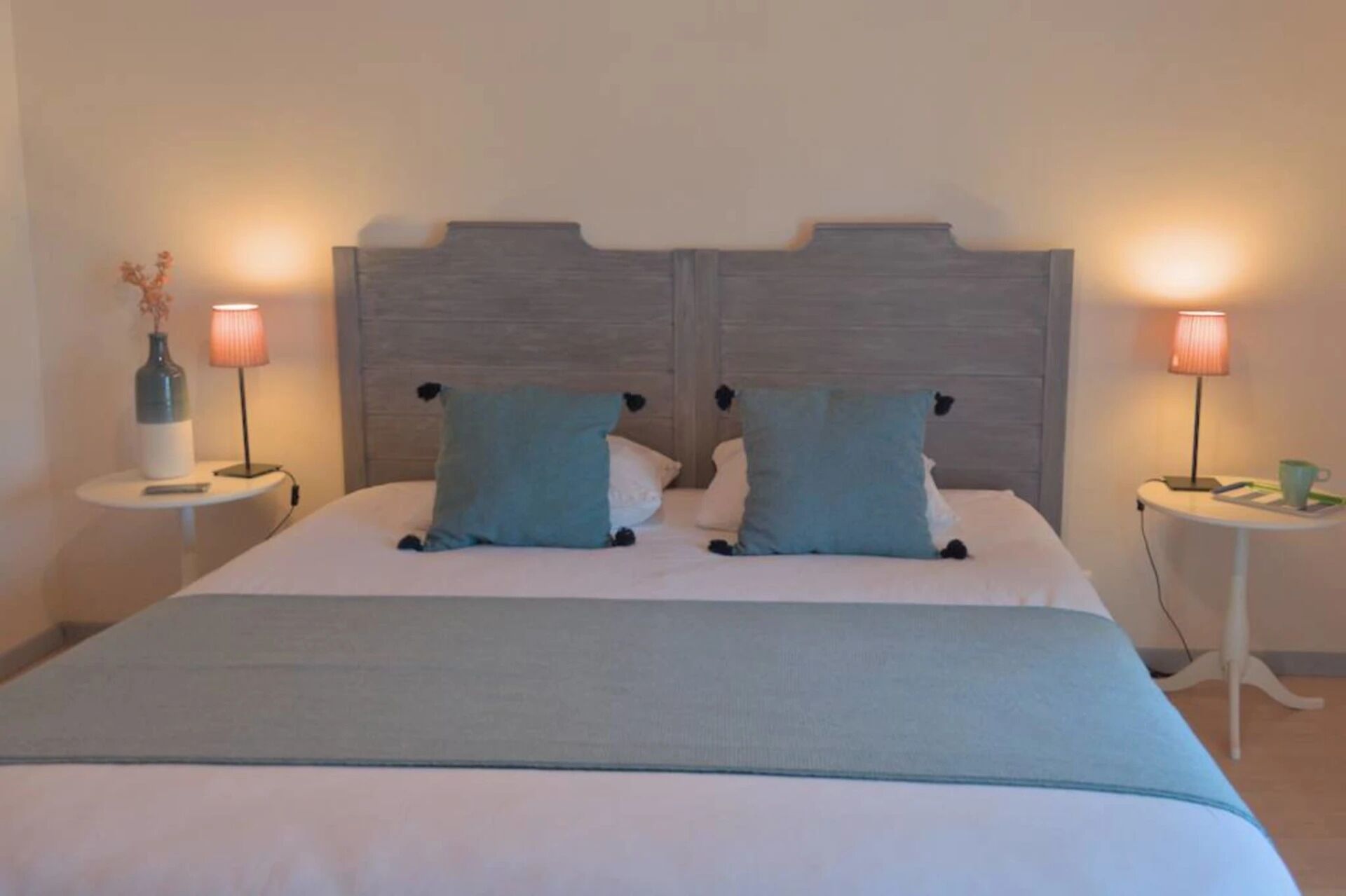 Ein Doppelbett mit Holzabdeckung, zwei Nachttische mit Lampen und eine Vase auf einem Tisch.