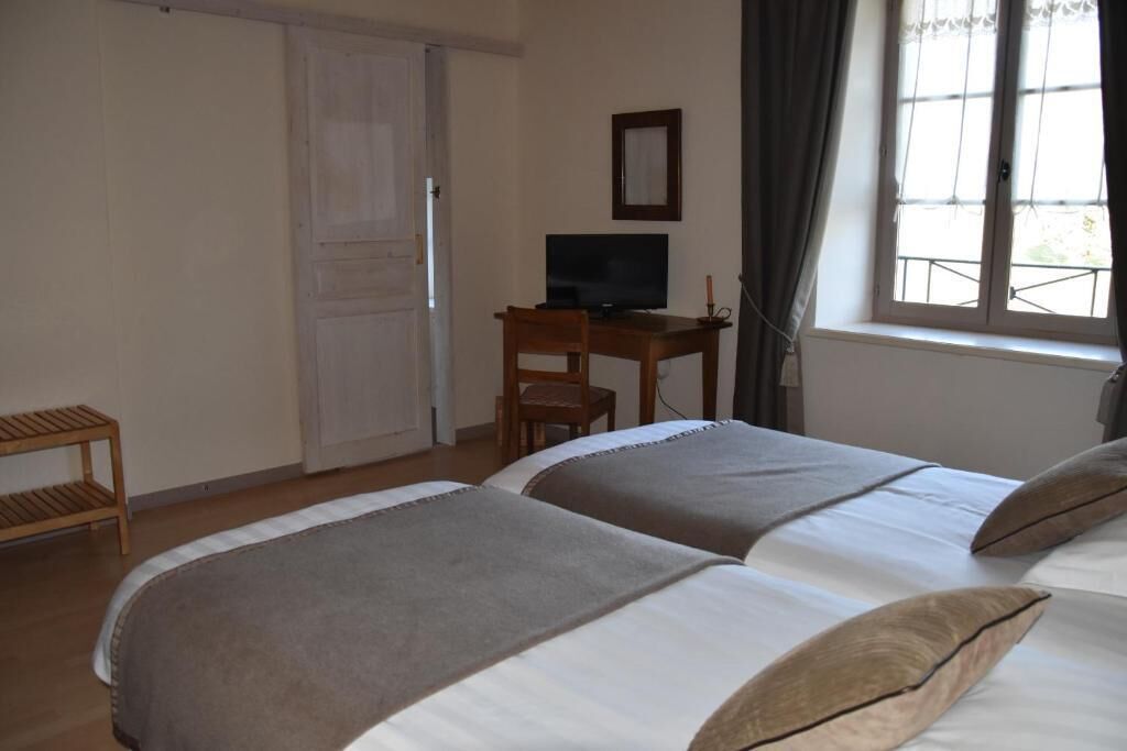 Habitación de hotel con dos camas, un escritorio con televisor, una ventana con cortinas y una silla de madera.