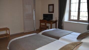 Habitación de hotel con dos camas, un escritorio con televisor, una ventana con cortinas y una silla de madera.