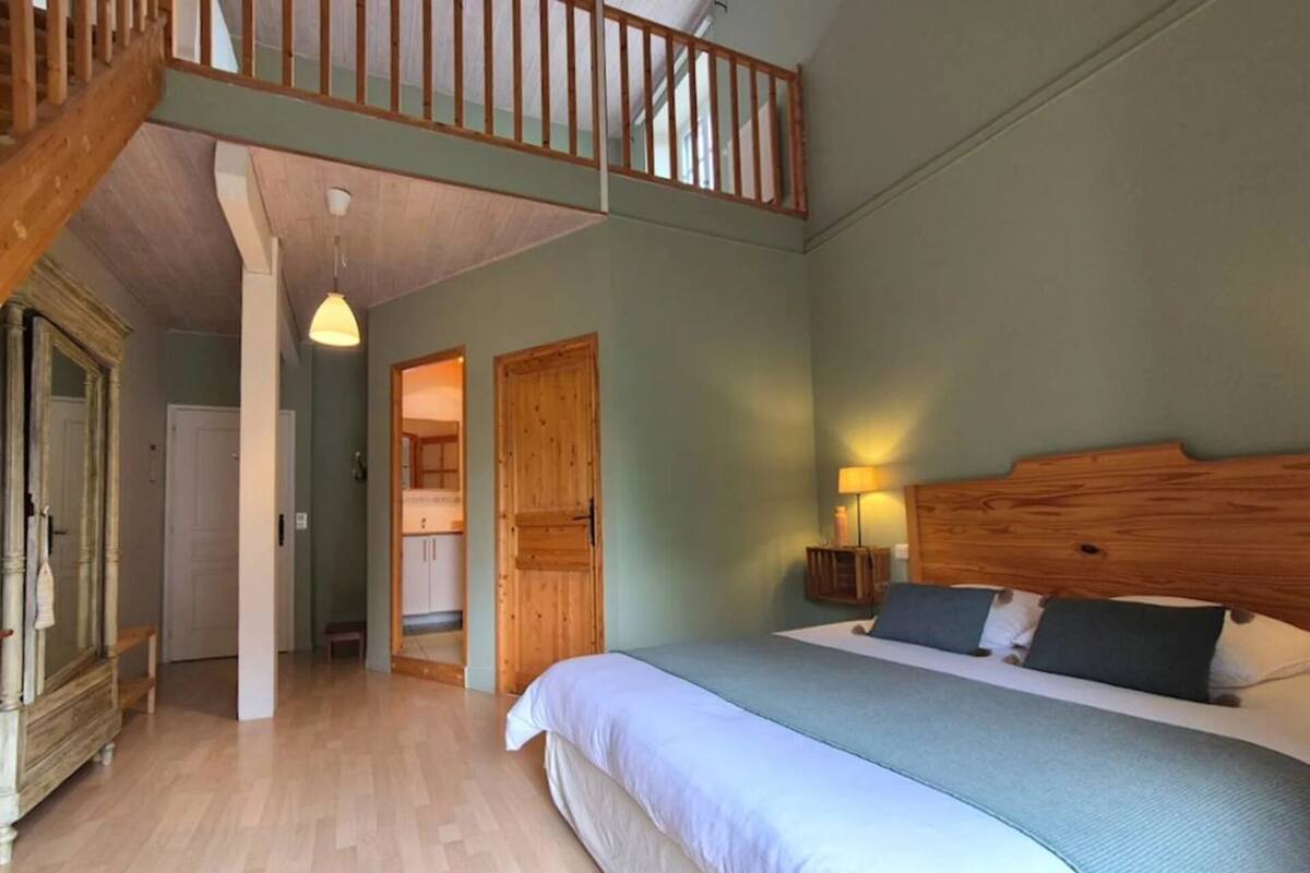 Ein Schlafzimmer mit einem großen Bett, einem Holzkopfteil, einem Nachttisch mit Lampe und Blick auf eine Küche durch eine offene Tür.