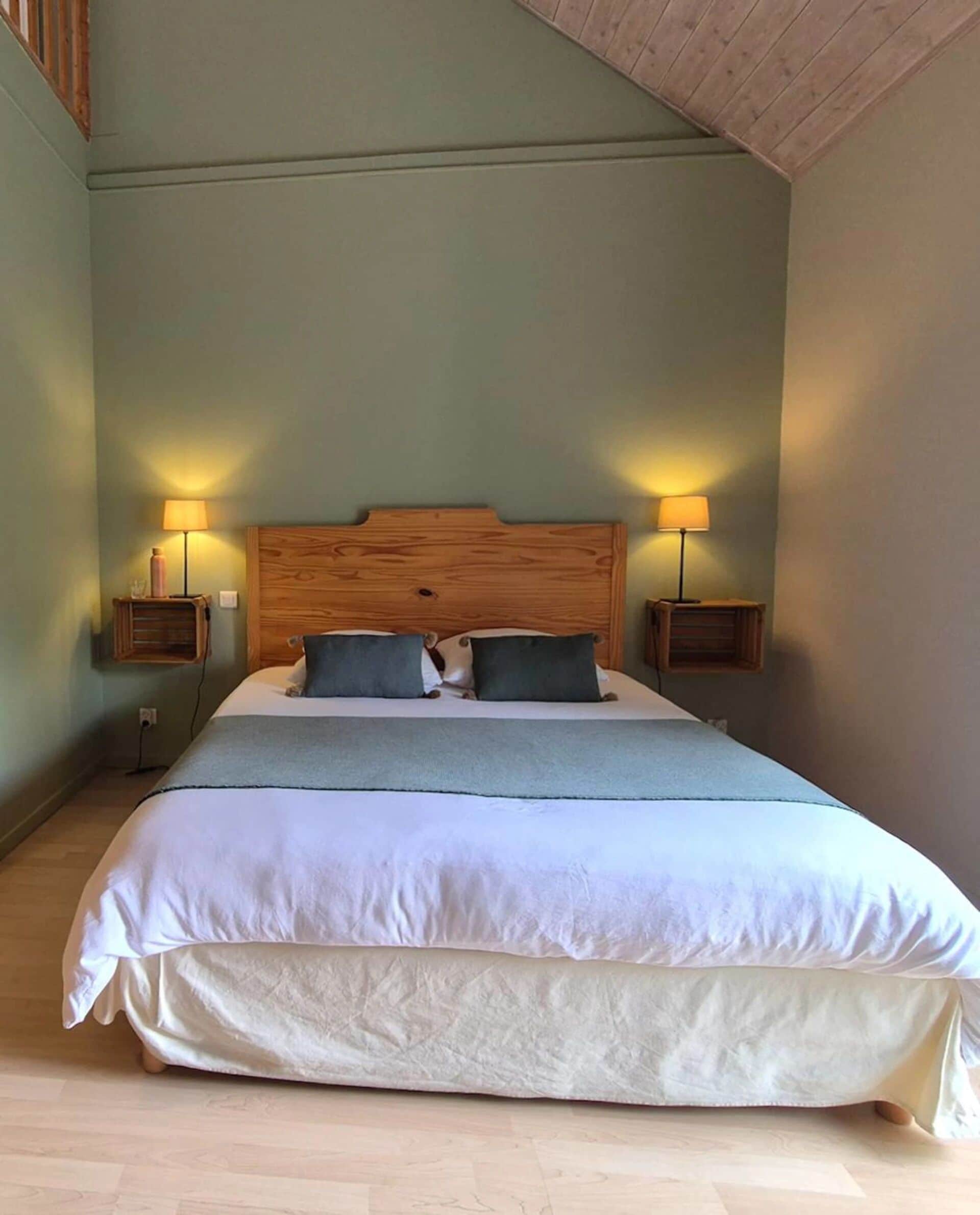 A large bed with a wooden headboard, two bedside lamps, and a grey throw blanket.