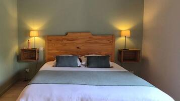 A large bed with a wooden headboard, two bedside lamps, and a grey throw blanket.